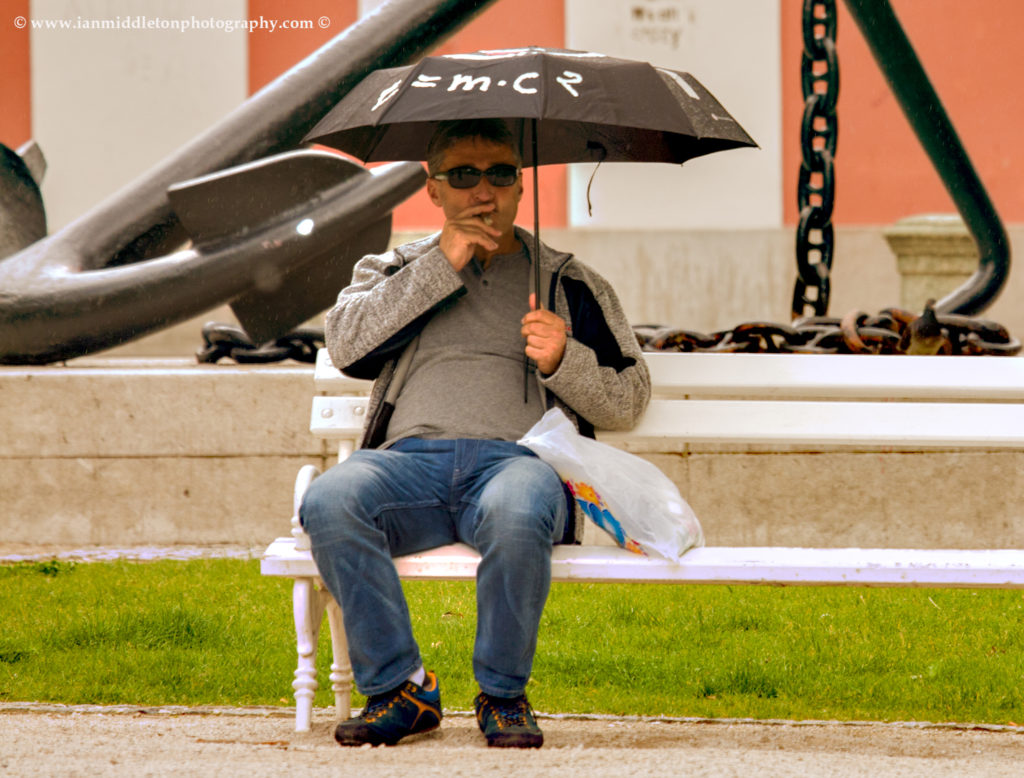 Man with umbrella with E = MC2 written on it in Kongresni Square, Ljubljana, Slovenia.