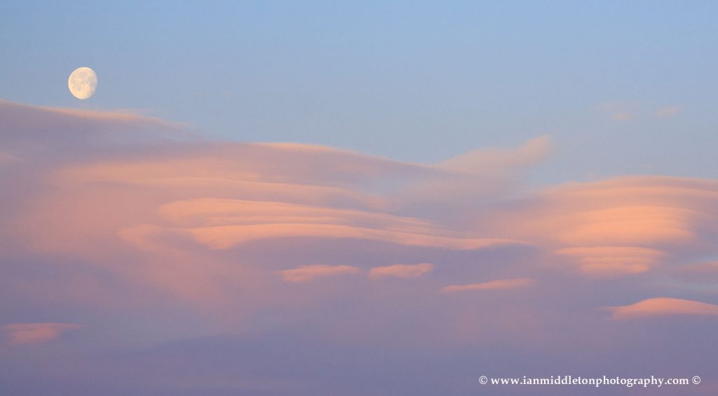 Lenticular cloud formation (Altocumulus lenticularis) at sunrise with the waning moon setting above then over residential area of Ljubljana taken from a sixth floor apartment , Slovenia